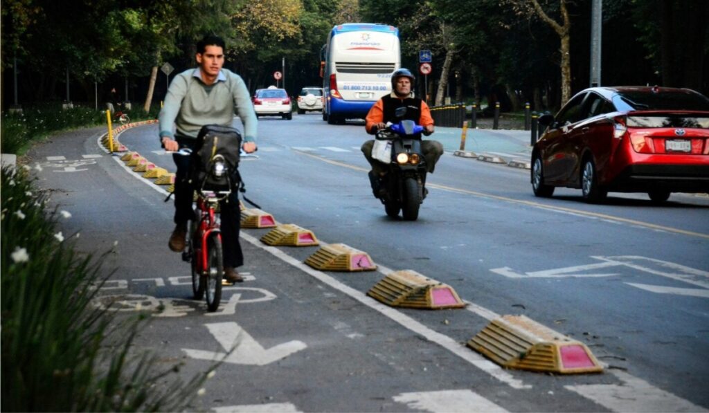 Ciclista y motociclista circulan junto a transporte público y automóviles en una vialidad de Ciudad de México.