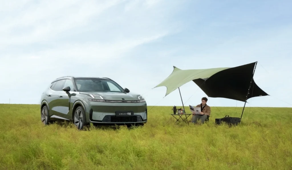 SUV híbrida enchufable Lynk & Co 08 de color verde estacionada en un campo abierto junto a un toldo de camping y una persona leyendo.