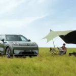 SUV híbrida enchufable Lynk & Co 08 de color verde estacionada en un campo abierto junto a un toldo de camping y una persona leyendo.