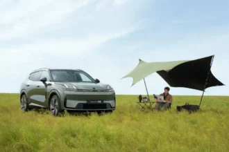 SUV híbrida enchufable Lynk & Co 08 de color verde estacionada en un campo abierto junto a un toldo de camping y una persona leyendo.