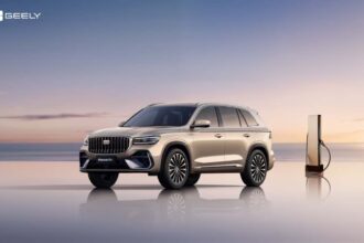 SUV Geely Monjaro EM-i híbrida enchufable color dorado estacionada junto a una estación de carga frente al mar.