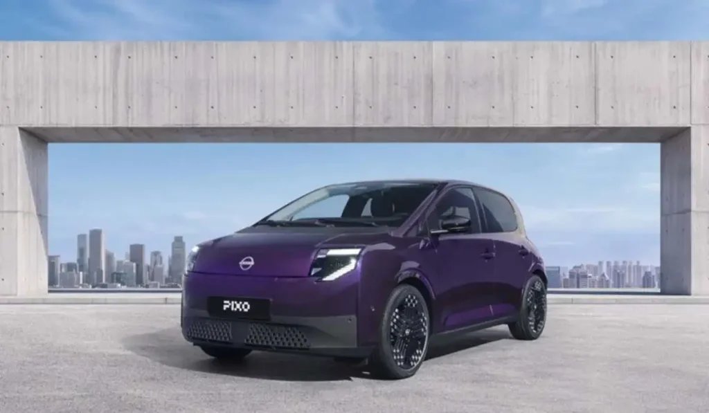 Vista frontal del coche urbano totalmente eléctrico Nissan PIXO en color morado oscuro estacionado frente a un paisaje urbano.