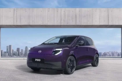 Vista frontal del coche urbano totalmente eléctrico Nissan PIXO en color morado oscuro estacionado frente a un paisaje urbano.