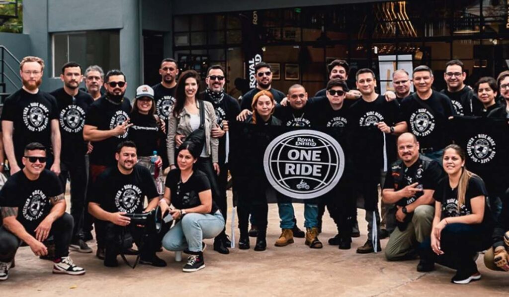 Grupo de motociclistas de la comunidad Royal Enfield posando juntos en camisetas negras con el logotipo oficial de One Ride.
