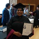 Egresada de la Universidad Nissan posando con birrete, toga y su título profesional durante la ceremonia de graduación.