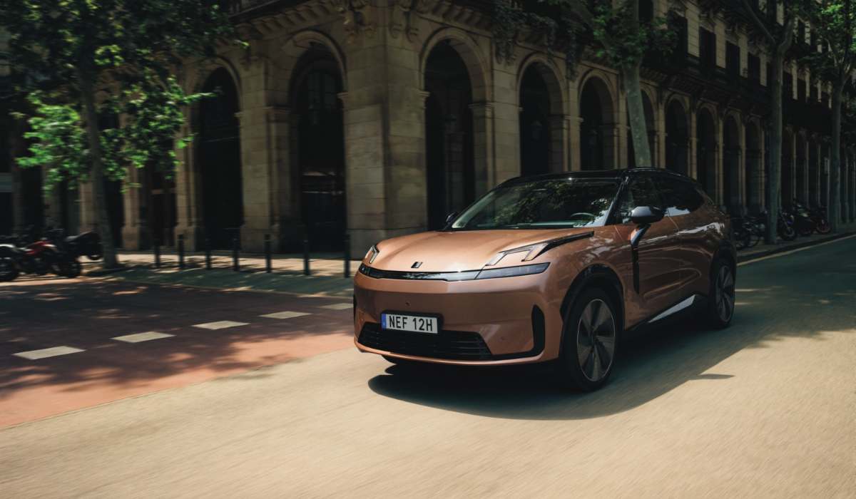 Vehículo eléctrico Lynk & Co en tono cobre circulando por una calle urbana europea arbolada con arquitectura clásica.