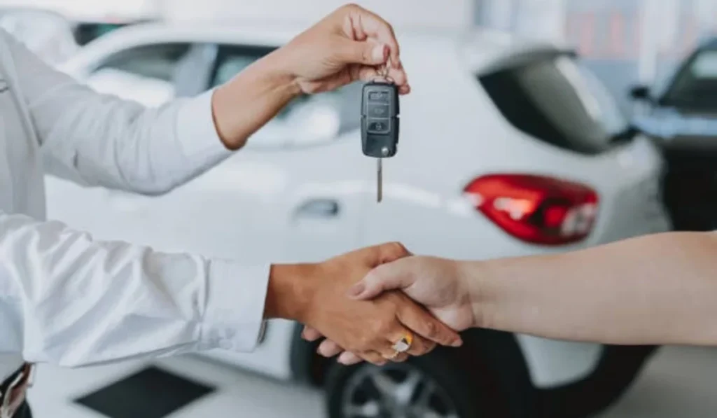 Asesor de ventas entregando la llave de un vehículo nuevo a un comprador mediante un apretón de manos en una agencia automotriz.