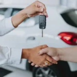 Asesor de ventas entregando la llave de un vehículo nuevo a un comprador mediante un apretón de manos en una agencia automotriz.