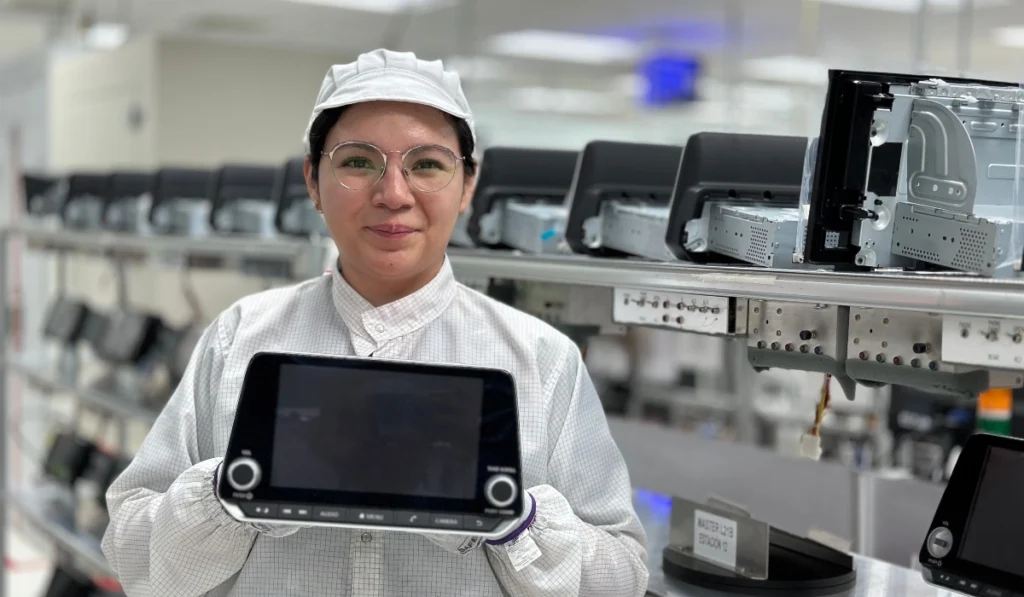 Colaboradora de FORVIA Clarion Electronics mostrando una pantalla de entretenimiento e infoentretenimiento automotriz en la planta de San Juan del Río, Querétaro.