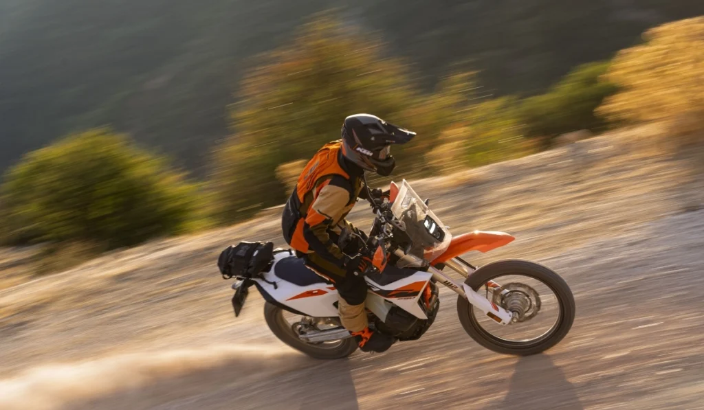 Motocicleta KTM 690 RALLY en movimiento por un camino de tierra fuera del asfalto con piloto equipado.