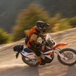 Motocicleta KTM 690 RALLY en movimiento por un camino de tierra fuera del asfalto con piloto equipado.