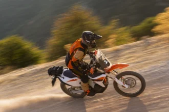 Motocicleta KTM 690 RALLY en movimiento por un camino de tierra fuera del asfalto con piloto equipado.