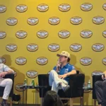 Franco Colapinto con gorra y uniforme de Alpine en un panel junto a David Geisen y Juan Lavista de Mercado Libre ante un fondo amarillo con logotipos de la marca.