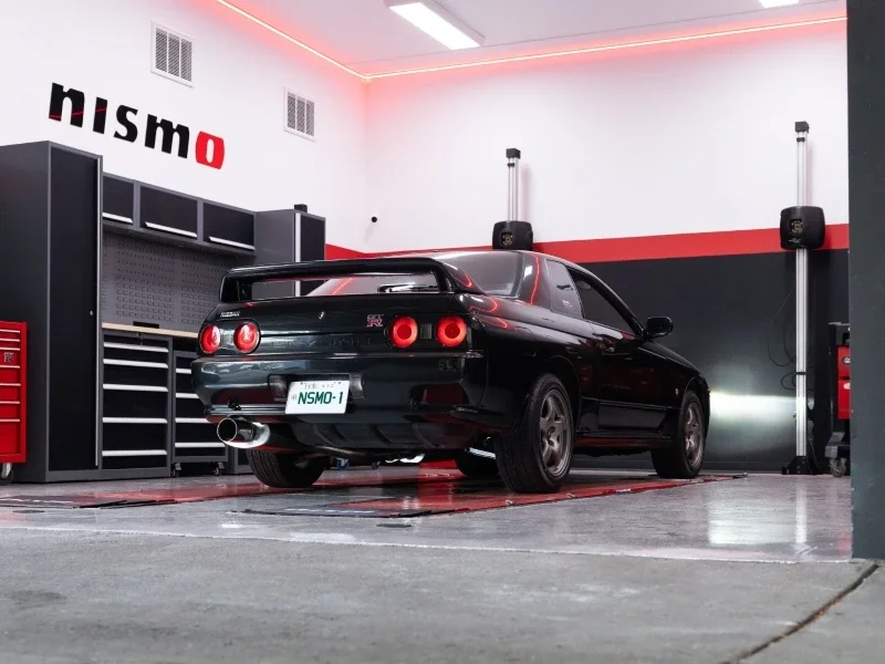 Nissan Skyline GT-R R32 color negro con luces traseras encendidas dentro de un taller especializado NISMO.