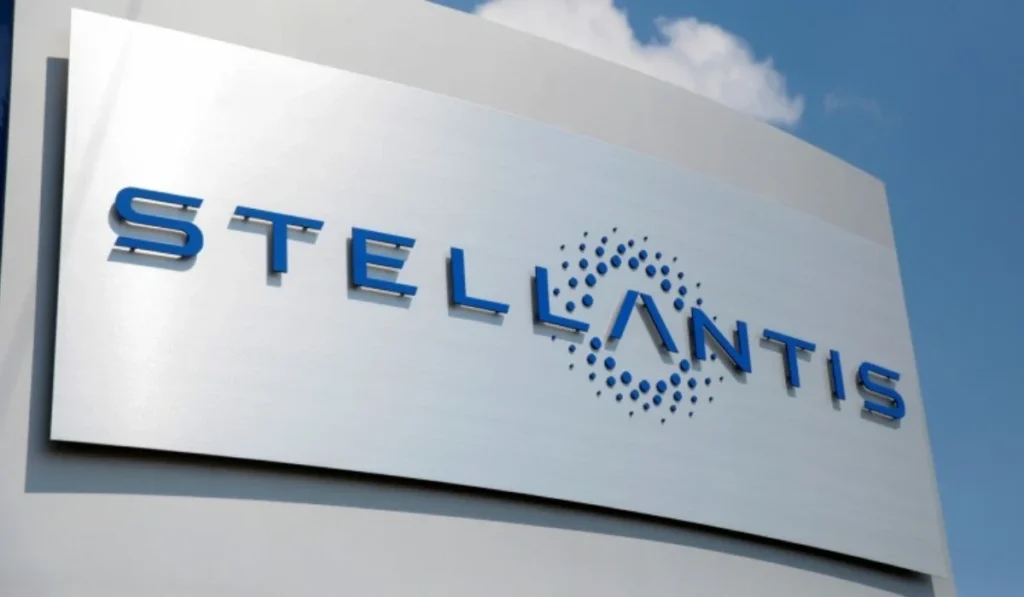 Letrero corporativo exterior de Stellantis en acabado metálico con letras azules sobre un fondo de cielo azul despejado.