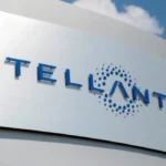 Letrero corporativo exterior de Stellantis en acabado metálico con letras azules sobre un fondo de cielo azul despejado.