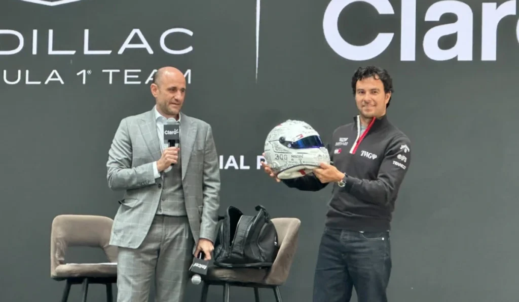 Sergio Checo Pérez sosteniendo su casco conmemorativo blanco por sus 300 carreras en F1 junto a un directivo en conferencia de prensa de Cadillac F1 Team.