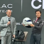 Sergio Checo Pérez sosteniendo su casco conmemorativo blanco por sus 300 carreras en F1 junto a un directivo en conferencia de prensa de Cadillac F1 Team.
